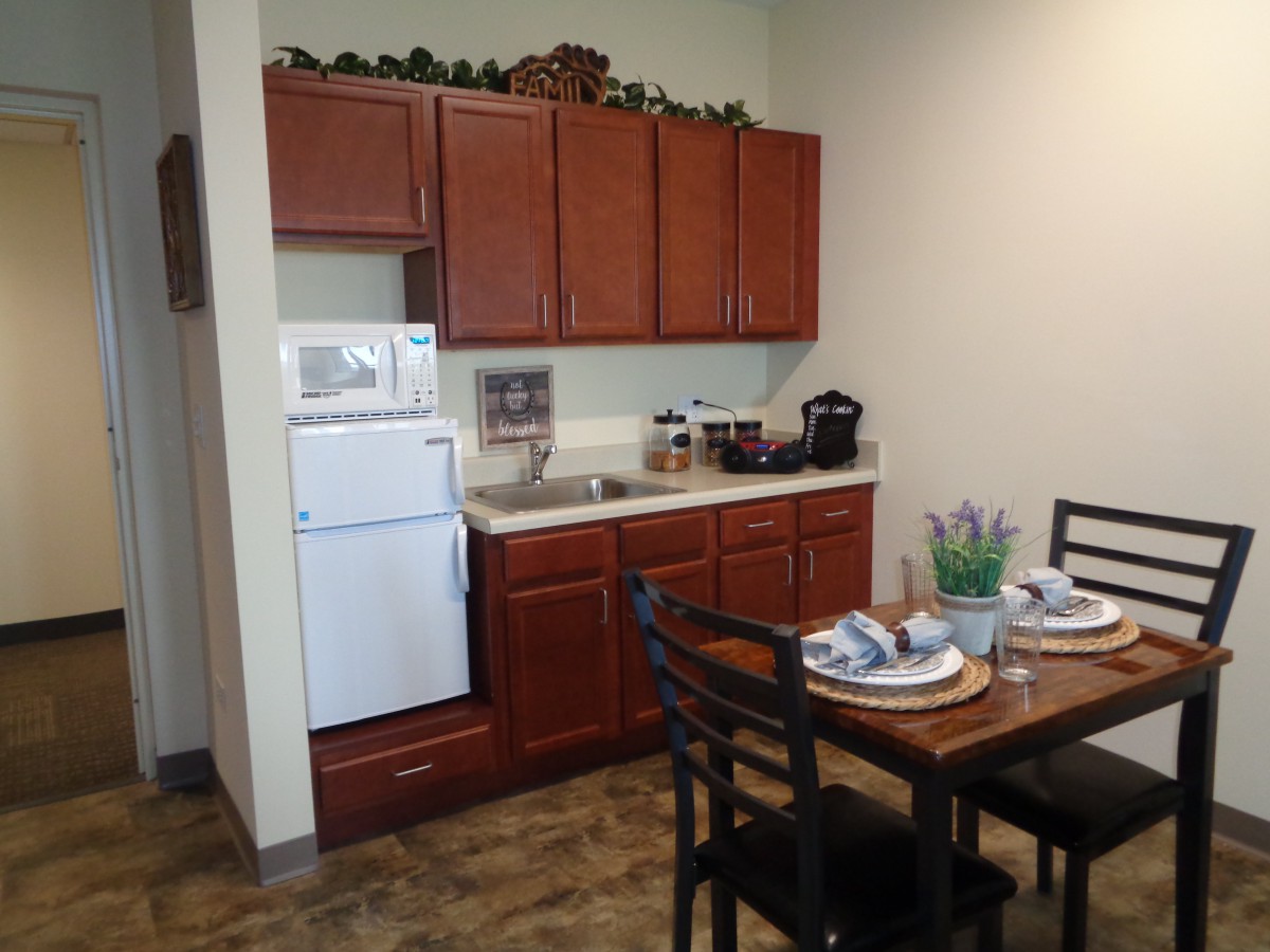 A compact kitchen and dining area with wooden cabinets, a refrigerator, and a table set for two.