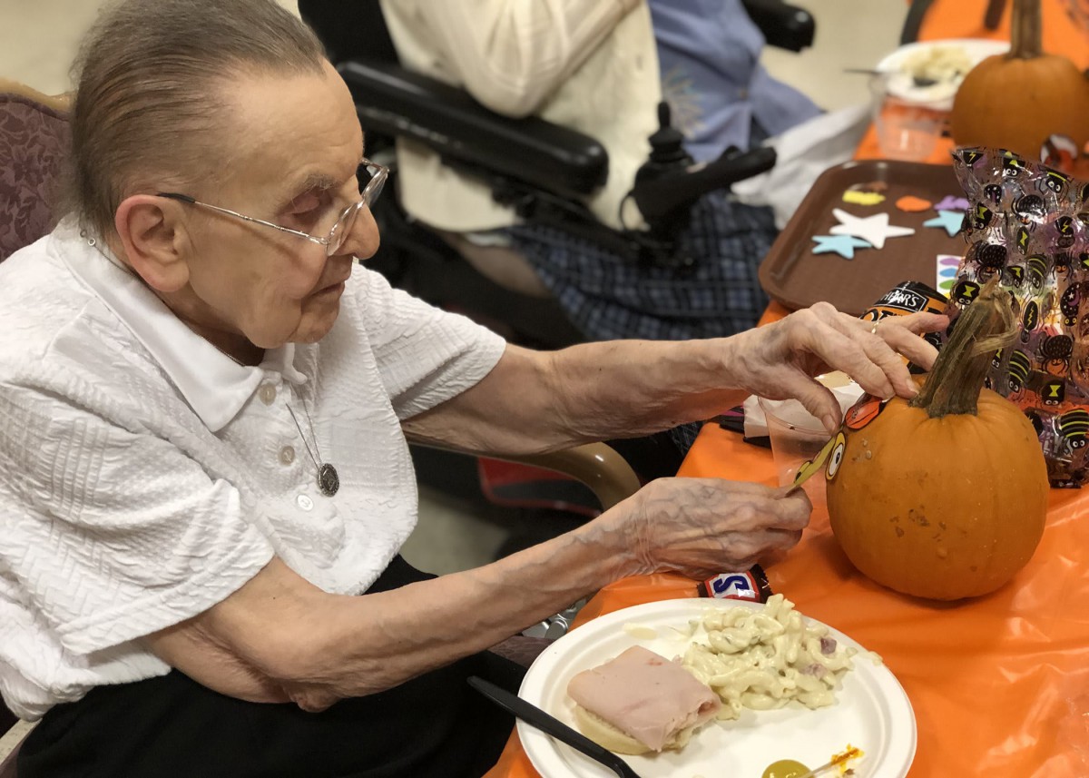 An elderly person participating in a pumpkin carving activity at a table decorated for autumn.