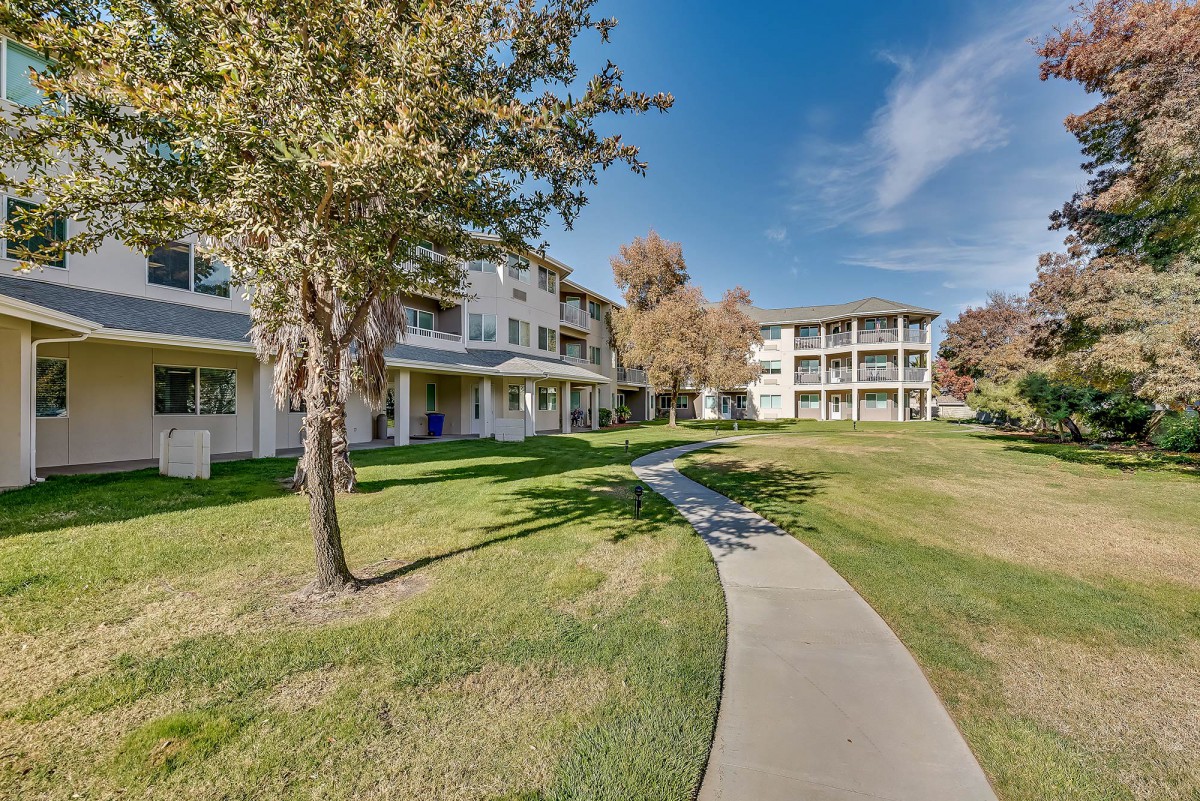 A scenic view of an apartment complex with a winding pathway surrounded by green grass and trees.