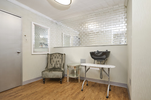 A stylish salon interior featuring a cozy chair, a wash station, and elegant wall tiles.