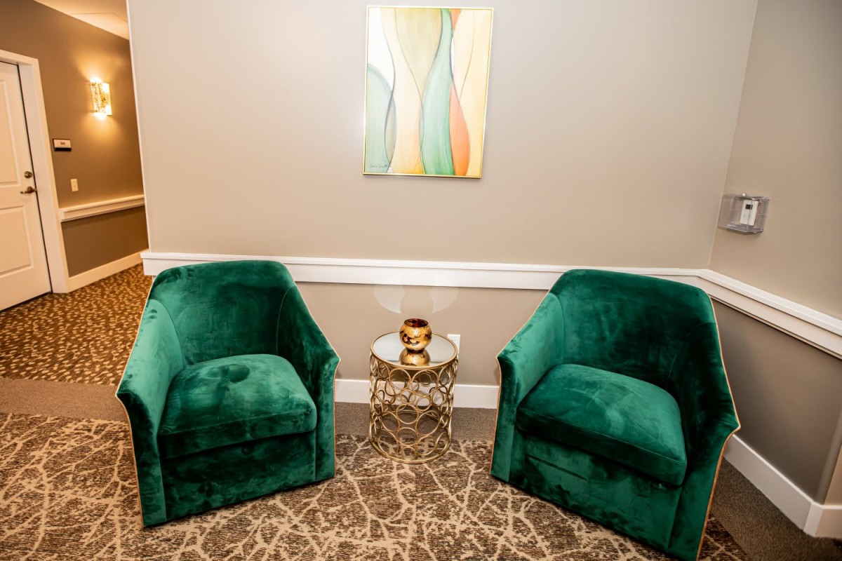 A cozy seating area with two green chairs and a small table between them, set against a neutral wall with abstract art.
