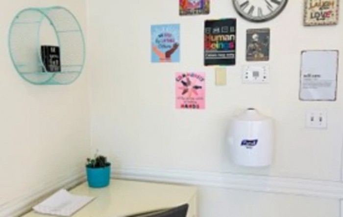 A small office corner with motivational posters, a clock, a desk with a cactus plant, and a hand sanitizer dispenser on the wall.
