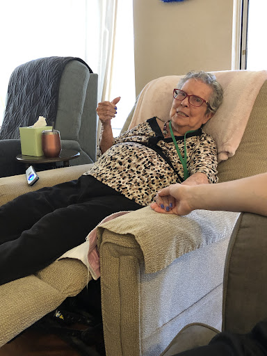 An elderly woman gives a thumbs up while relaxing in a recliner chair.