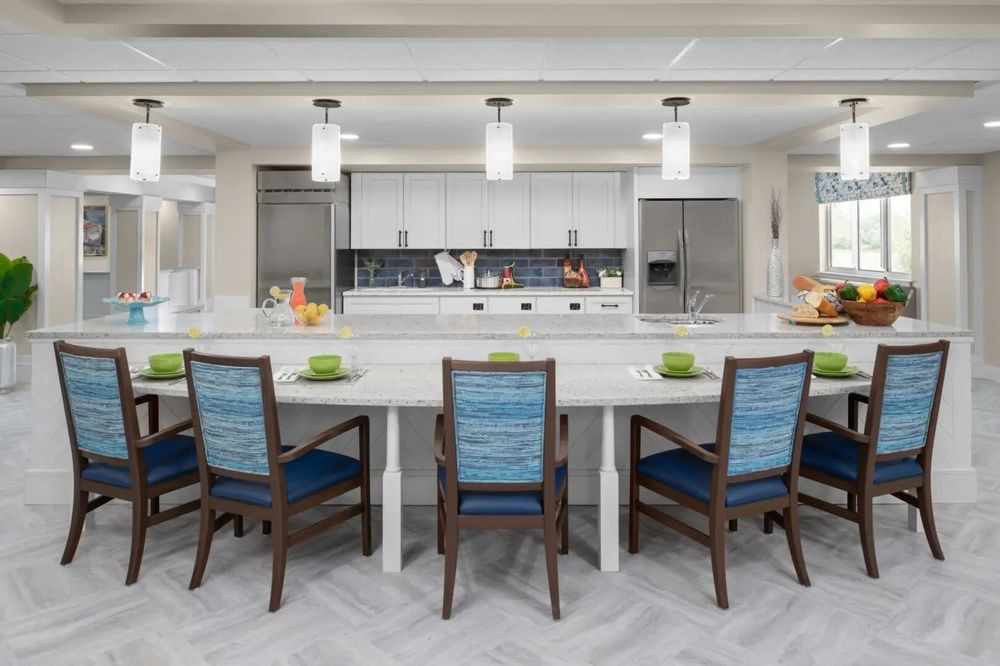 A modern kitchen with a spacious countertop and stylish dining chairs, featuring sleek appliances and pendant lighting.