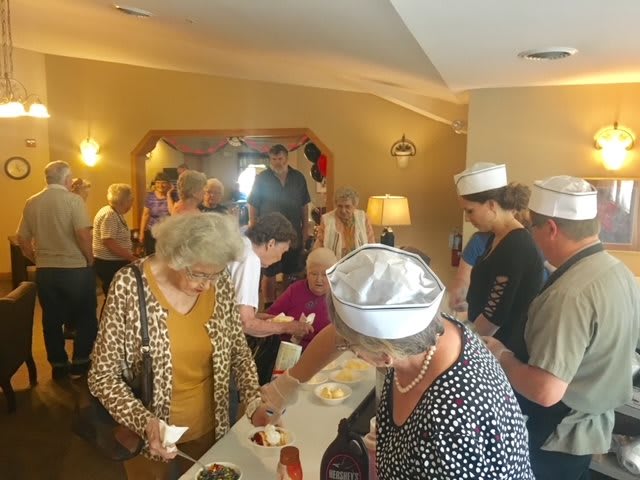A group of elderly individuals gather indoors for a social event, enjoying food and conversation.