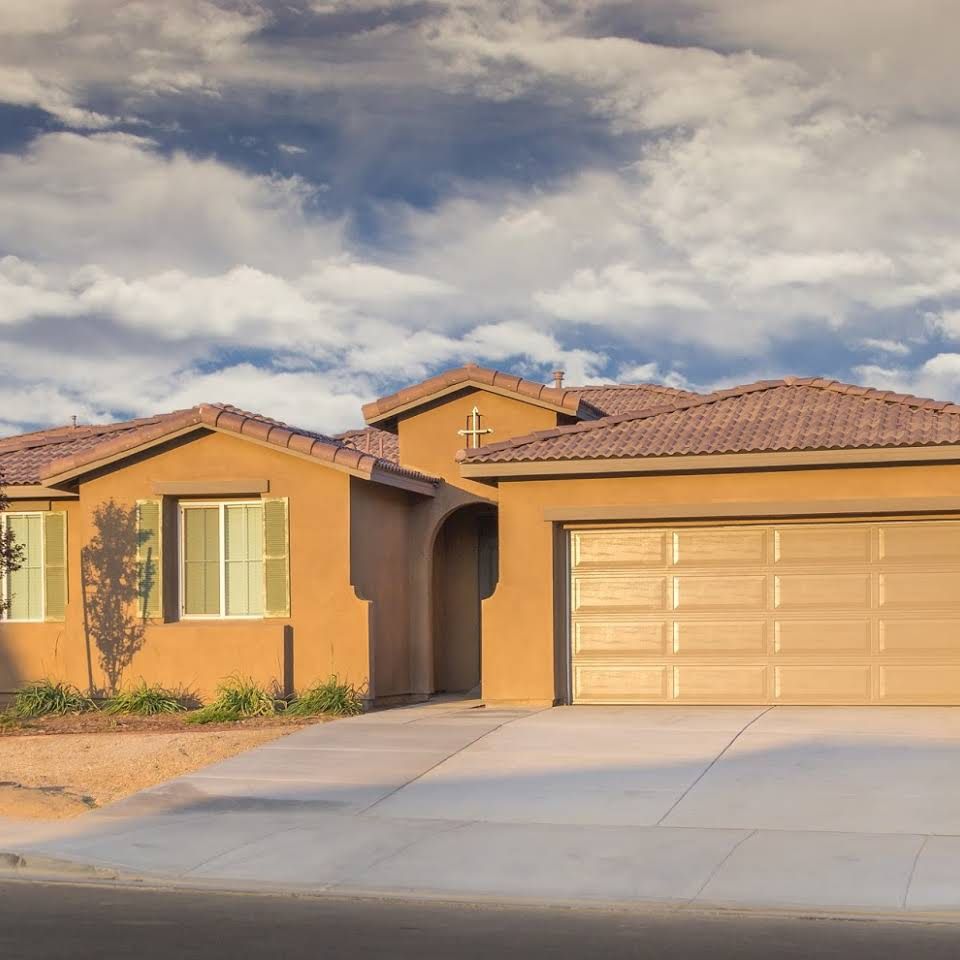 A suburban house with a two-car garage and a tile roof under a partly cloudy sky.