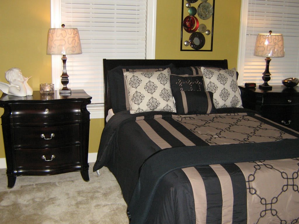 A stylishly furnished bedroom featuring a bed with patterned bedding, matching cushions, and a dark wood nightstand with lamps.