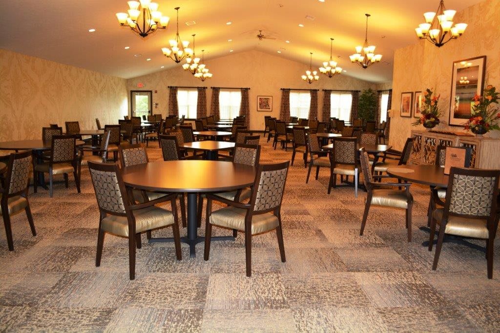 An empty dining room with neatly arranged tables and chairs, illuminated by chandeliers.
