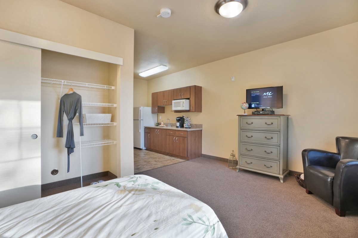 A cozy hotel room featuring a bed, a small kitchenette, and a television atop a dresser.