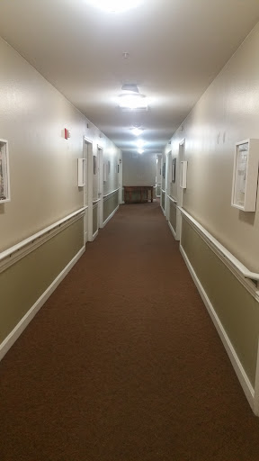 A well-lit corridor with beige walls and carpet, featuring several doors on either side.