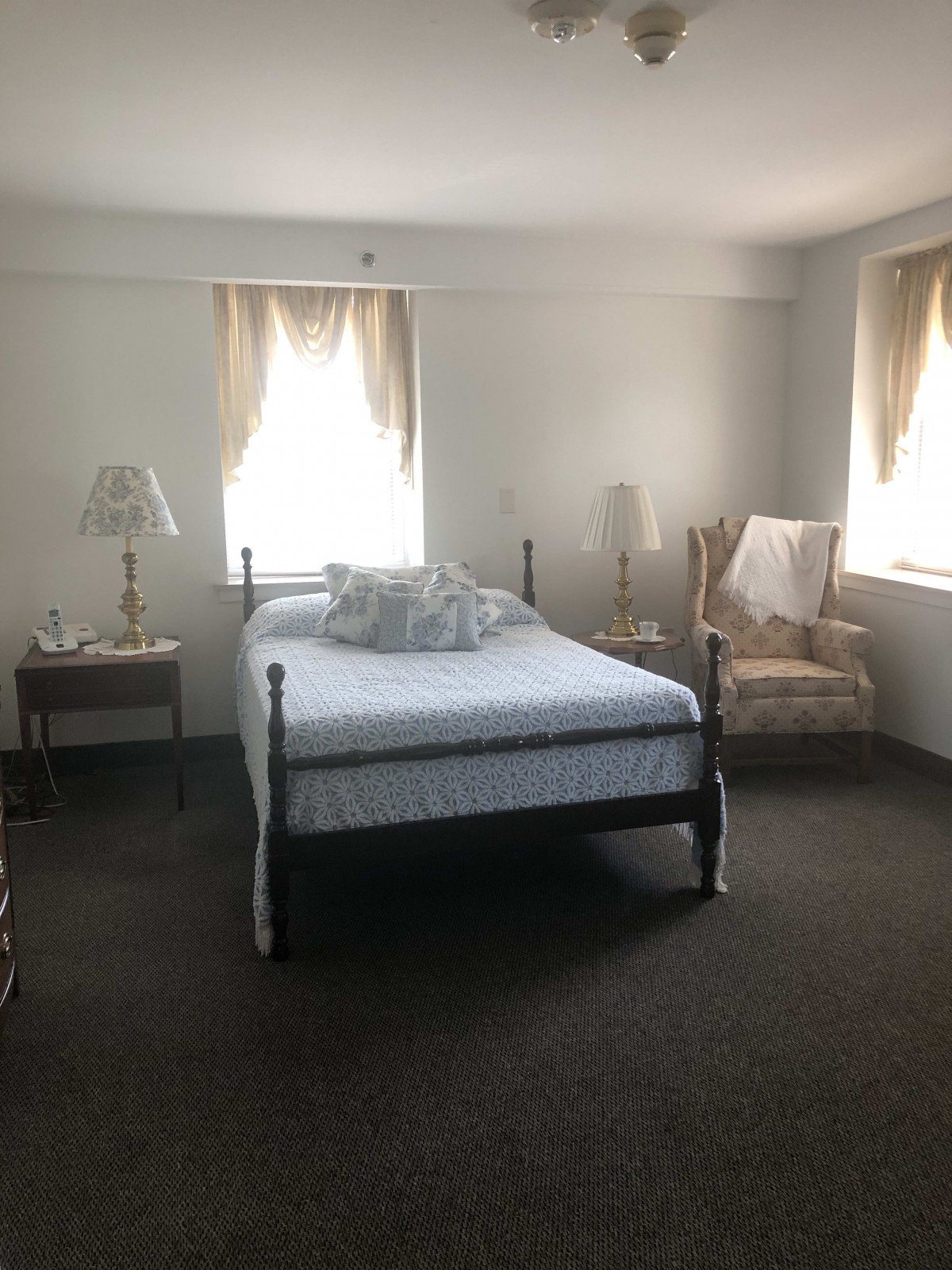 A cozy bedroom with a bed, two bedside tables with lamps, and soft natural light filtering through the windows.