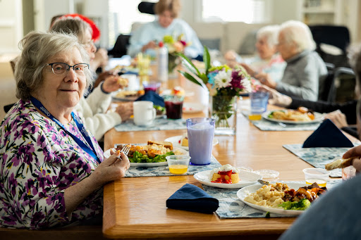 A group of seniors enjoying a communal meal together at a dining table, surrounded by flowers and delicious dishes.