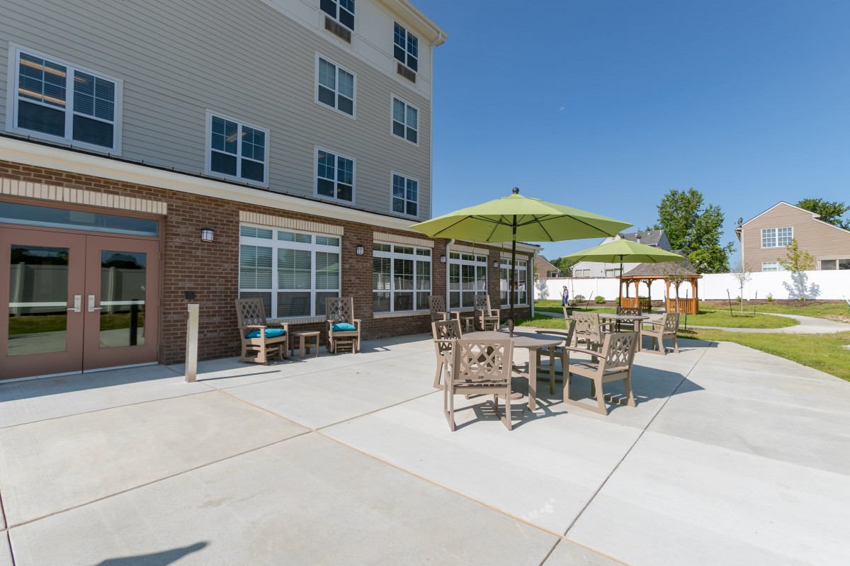 An outdoor patio area with tables, chairs, and umbrellas outside a building on a sunny day.