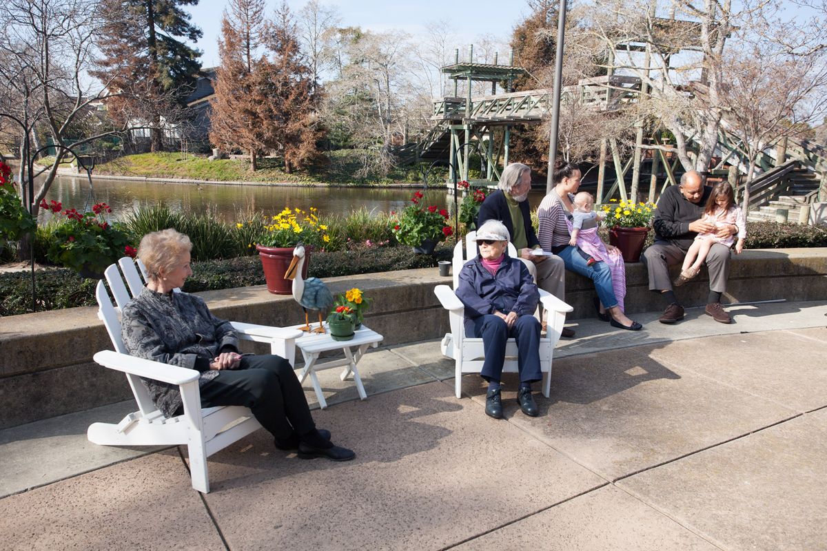 A group of people sitting and socializing in a park on a sunny day.