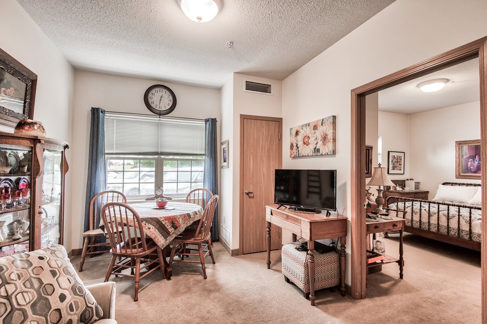Cozy dining area with a table set for four, featuring a wall-mounted clock and a television in an adjoining living space.