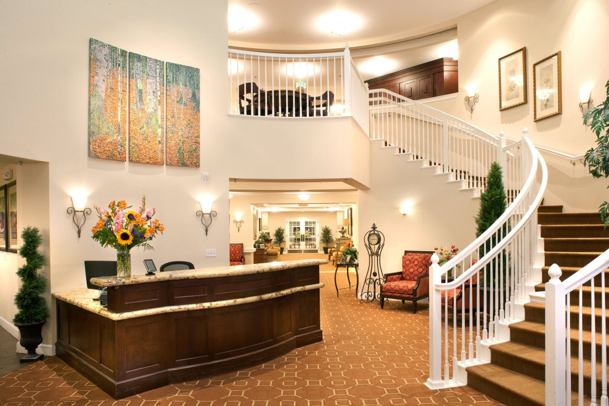 A spacious hotel lobby featuring a reception desk, grand staircase, and comfortable seating areas.