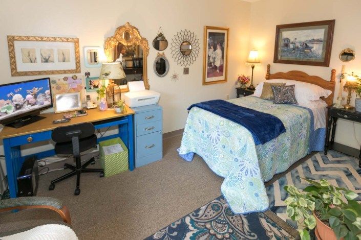 A cozy bedroom with a neatly made bed, a desk area, and various decorative elements on the walls.
