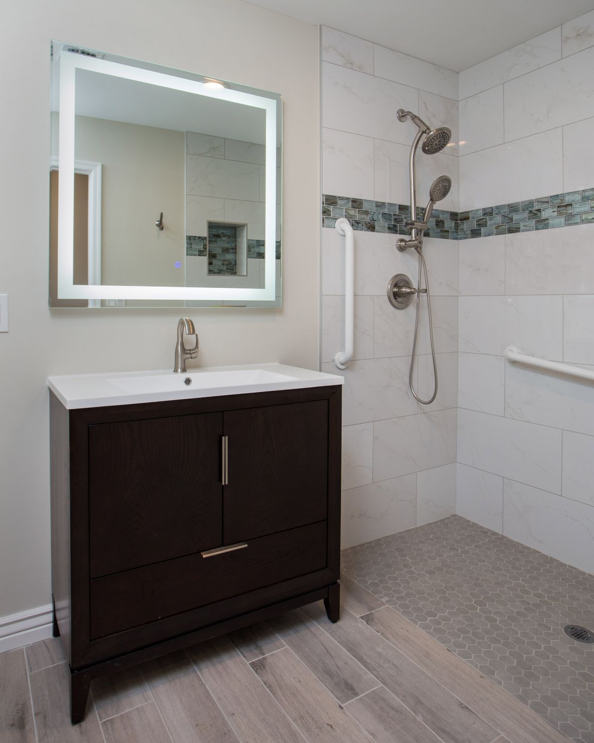 A modern bathroom with a sleek vanity, illuminated mirror, and tiled walk-in shower.