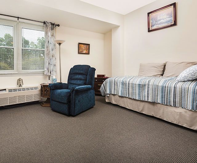 A cozy bedroom featuring a single bed and a blue armchair with natural light coming through the window.