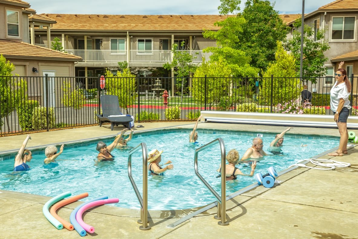 A group of seniors participating in a water exercise class at an outdoor swimming pool.