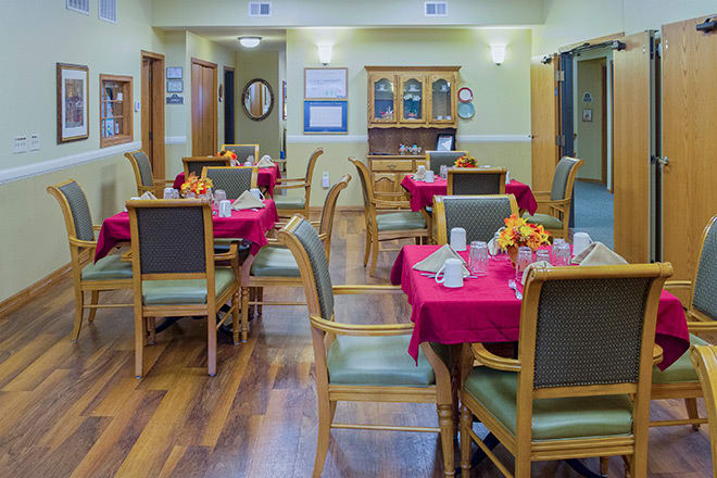 A cozy dining room with tables set up for guests, featuring red tablecloths and elegant decor.
