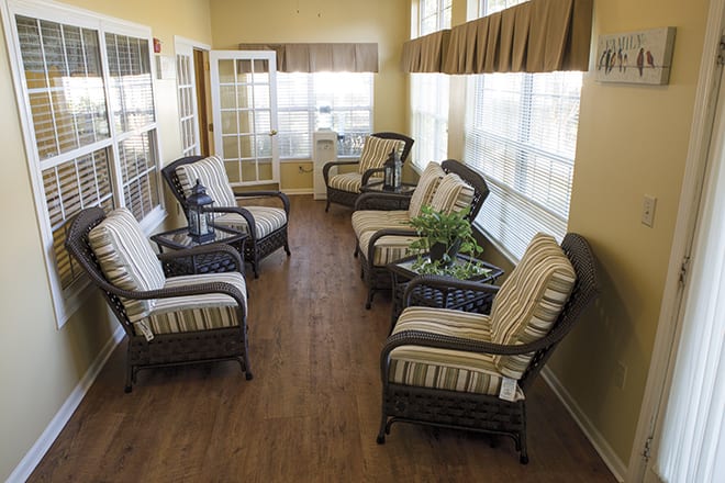 A cozy sunroom with wicker chairs and cushions, surrounded by large windows.
