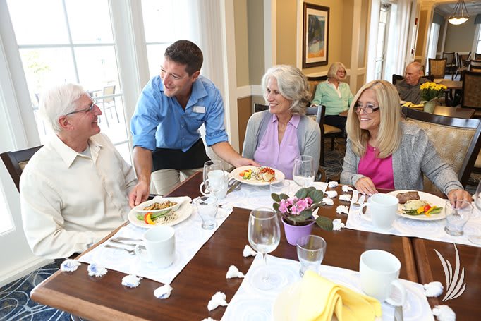 A waiter serves a meal to a group of elderly people enjoying a conversation at a restaurant.