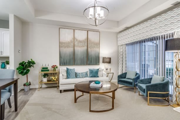 A modern living room with stylish furniture, including a sofa and armchairs, centered around a coffee table, decorated with artwork and illuminated by a chandelier.