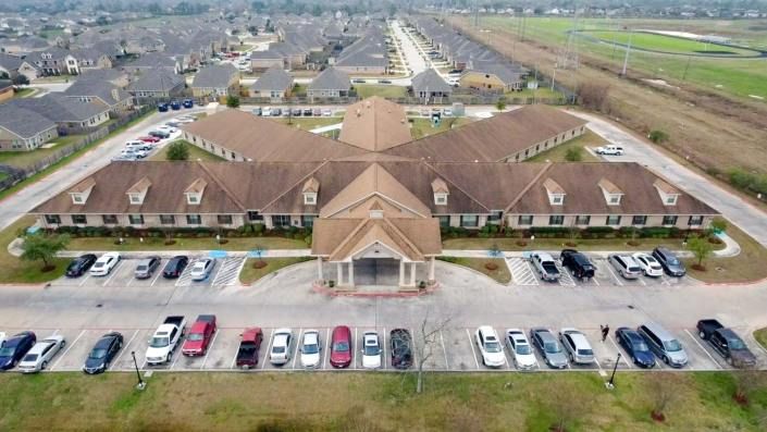 Aerial view of a large building with a surrounding parking lot in a suburban area.