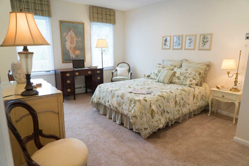 A cozy bedroom featuring a floral bedspread, wooden desk, and plush carpeting.