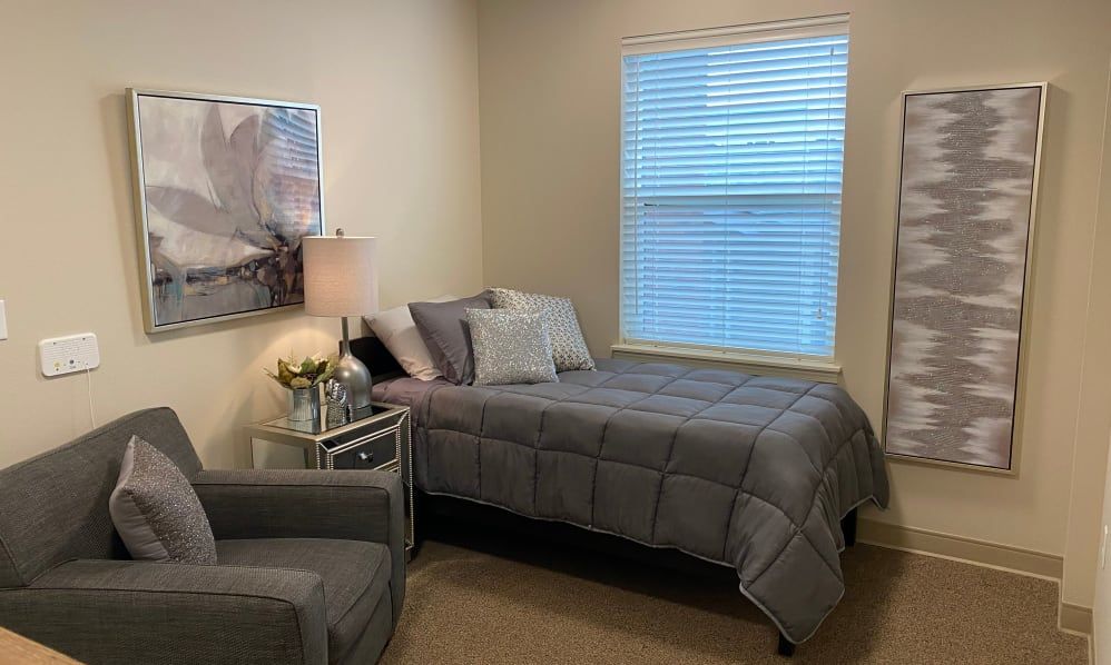 A cozy and minimalist bedroom featuring a neatly made bed, a comfortable chair, and soft lighting from a bedside lamp.