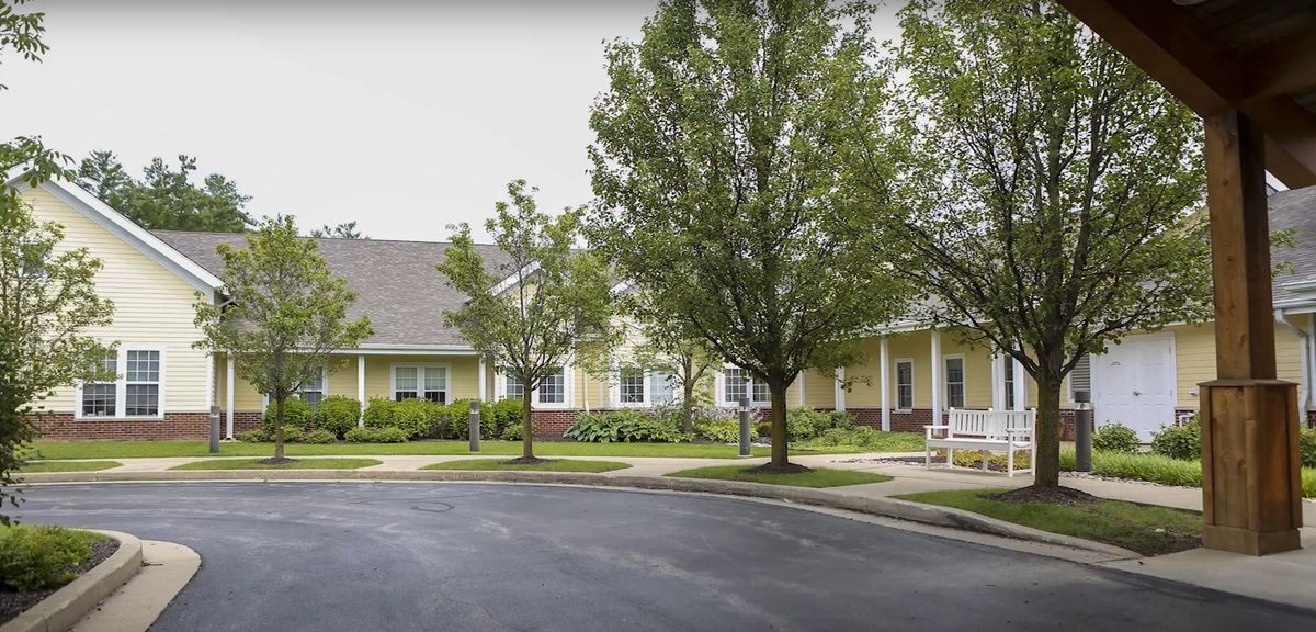 A suburban residential building surrounded by trees and a paved road.