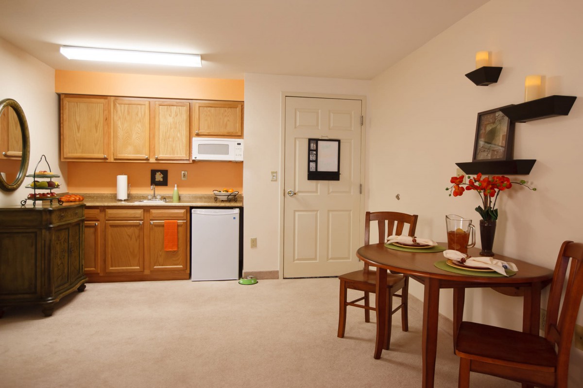 A cozy apartment kitchen and dining area featuring wooden cabinets and a small table with chairs.
