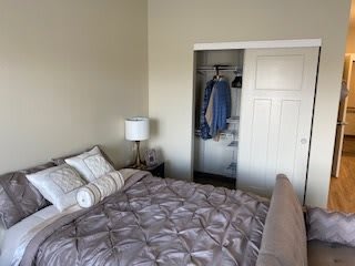 A cozy bedroom with a neatly made bed, pillows, and an open closet.