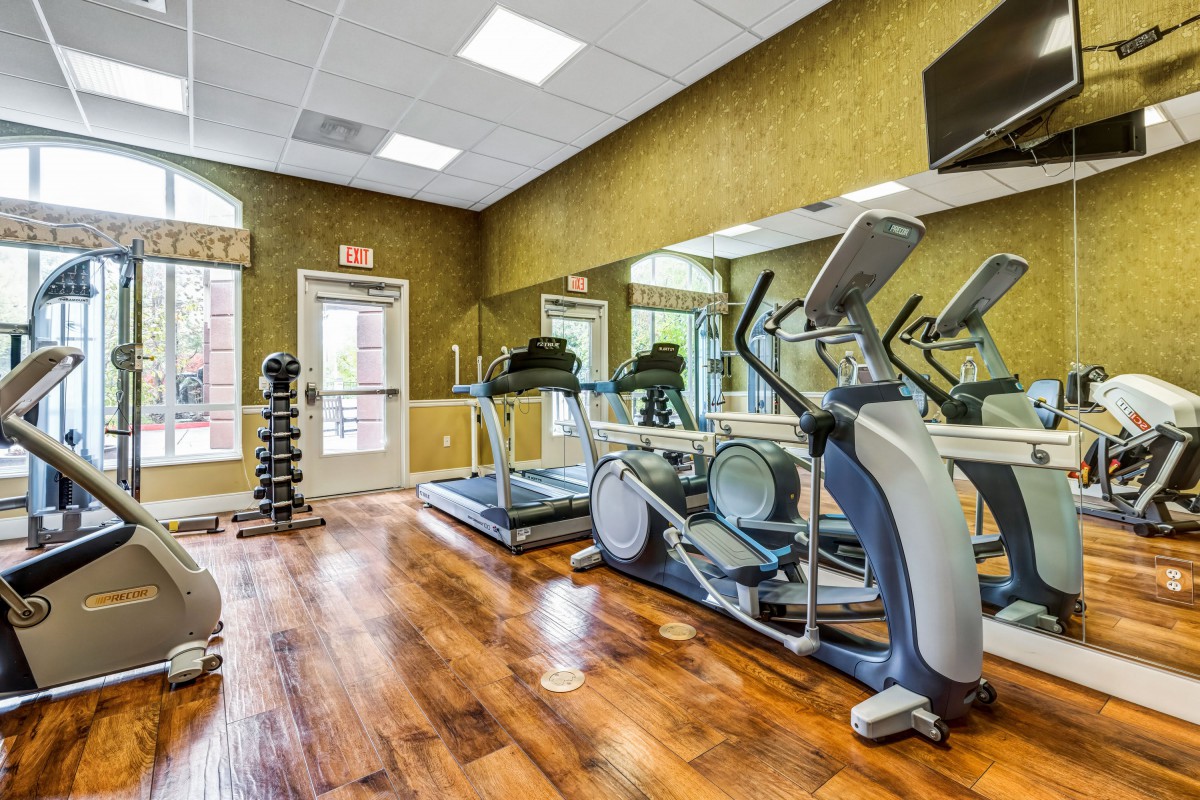 A well-equipped gym with treadmills, an elliptical machine, and a set of dumbbells on a wooden floor.