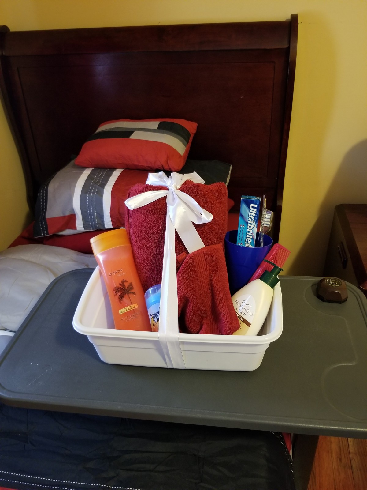 A gift basket filled with toiletries and towels, adorned with a white ribbon, placed on a bed in a cozy bedroom setting.