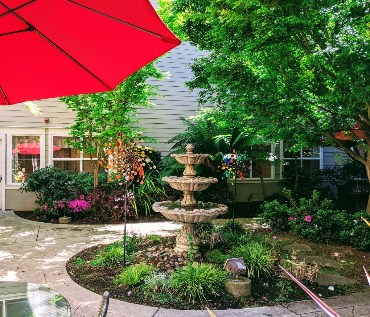 A beautifully landscaped garden patio with a central fountain and a red umbrella providing shade.