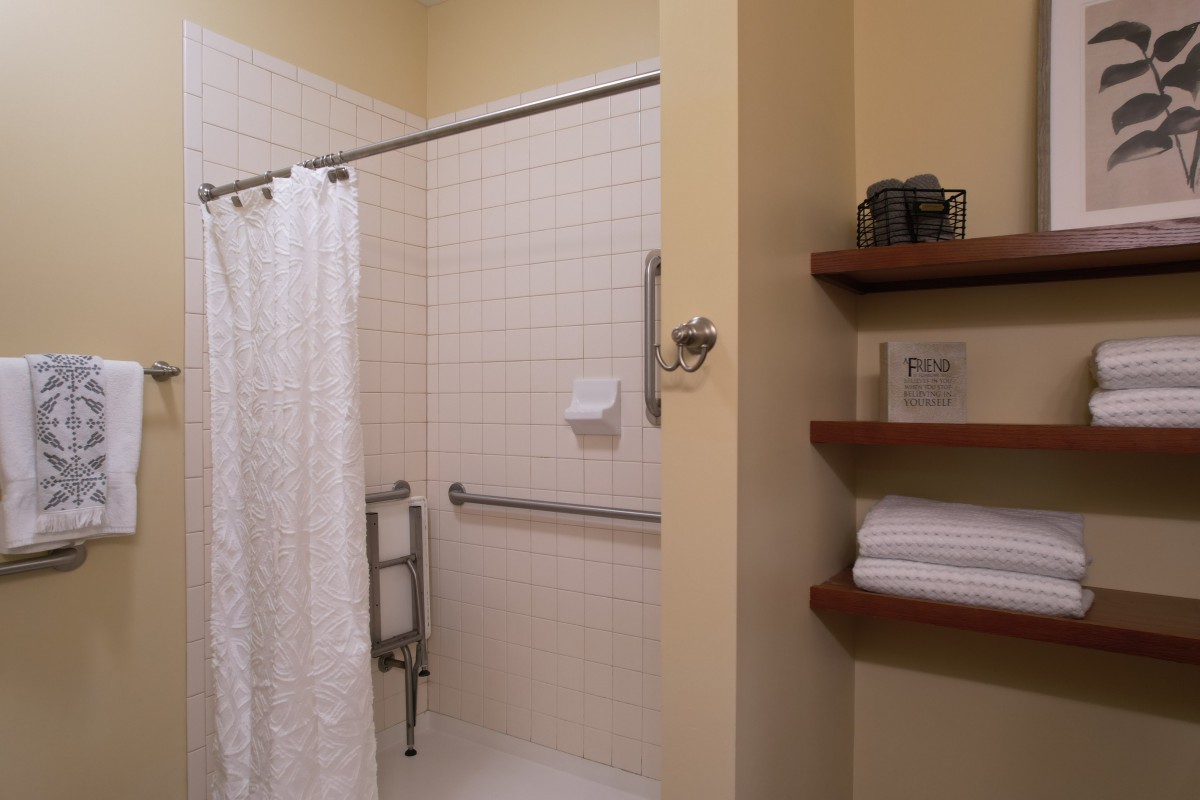 A clean and organized bathroom with a shower, equipped with grab bars and neatly arranged towels on shelves.