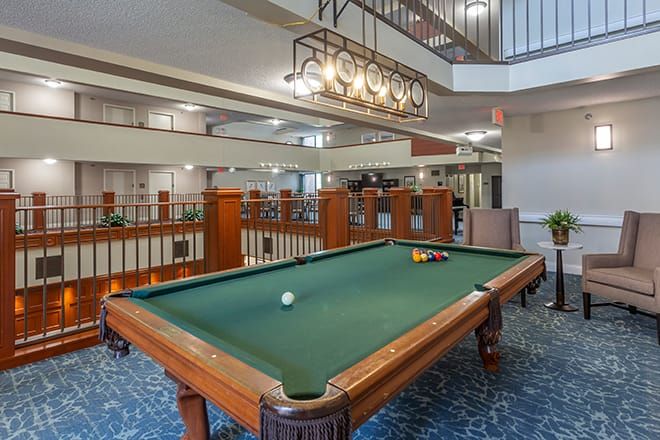 A spacious recreation area featuring a billiards table and comfortable seating, illuminated by an elegant lighting fixture.