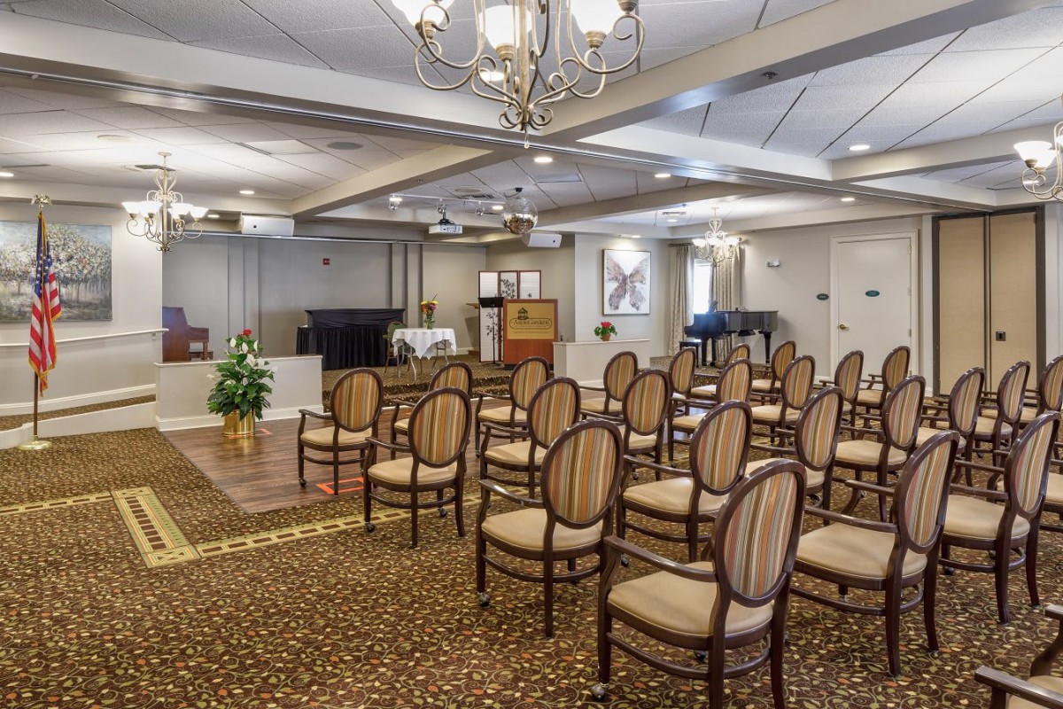 An interior view of a funeral home setup with rows of chairs, chandeliers above, and a podium at the front.