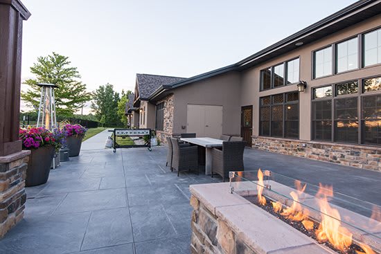 A modern outdoor patio area with a fire pit and furniture, set against a landscaped garden.