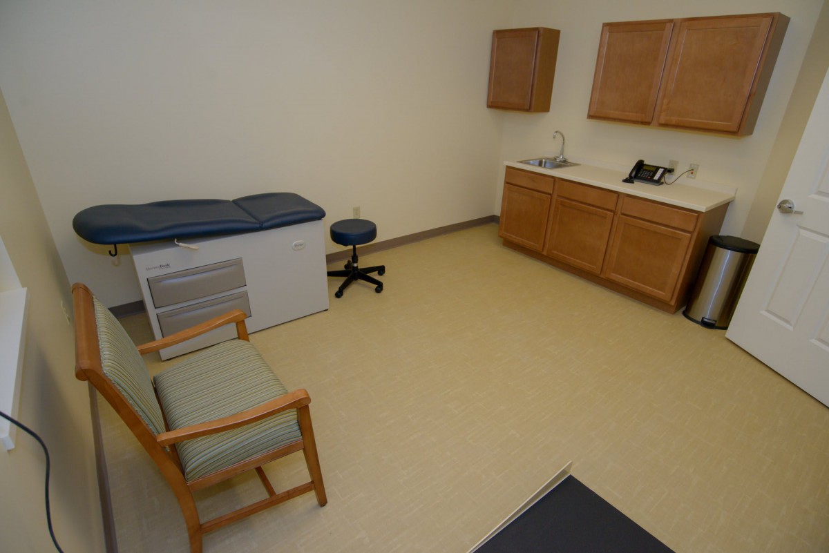 A small medical examination room with an exam table, chair, and cabinets.