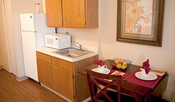 A cozy kitchen and dining area with wooden cabinets, a microwave, a sink, and a small table set for two.