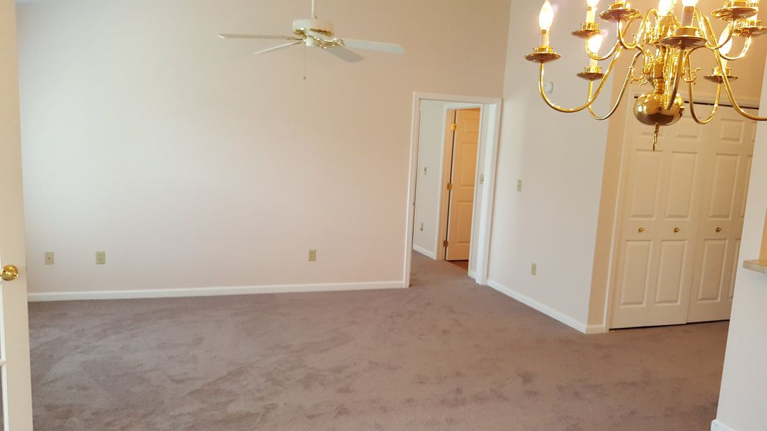 An empty room with beige walls, carpet flooring, a ceiling fan, and a chandelier.