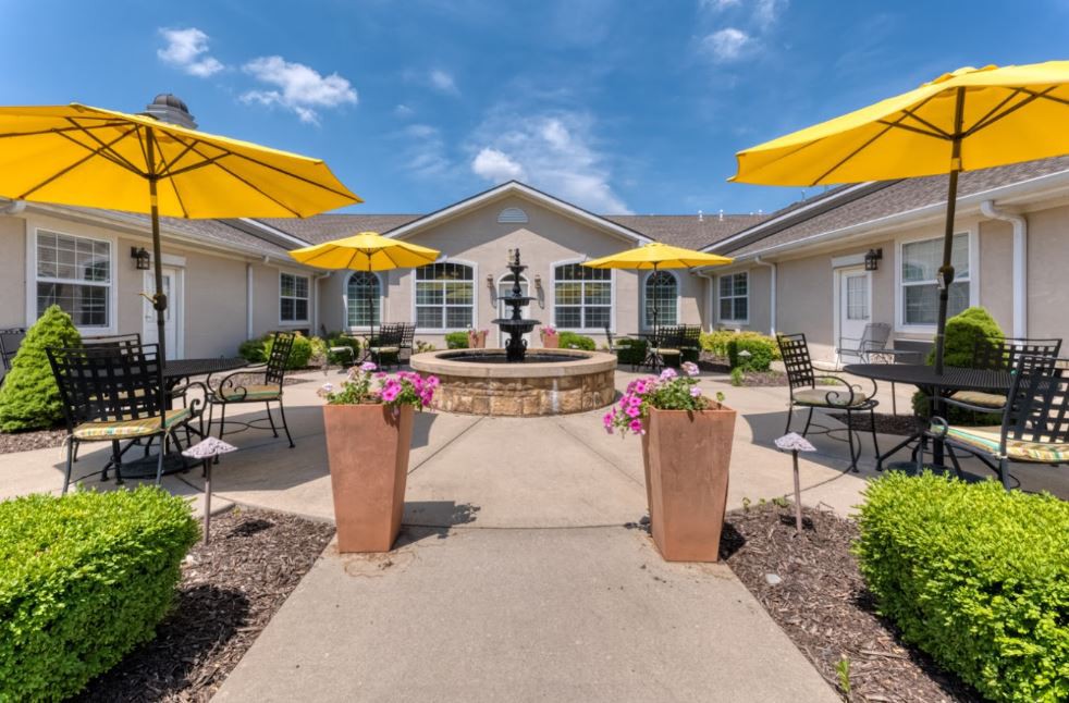 A sunny courtyard with a central fountain, surrounded by yellow umbrellas and outdoor seating.