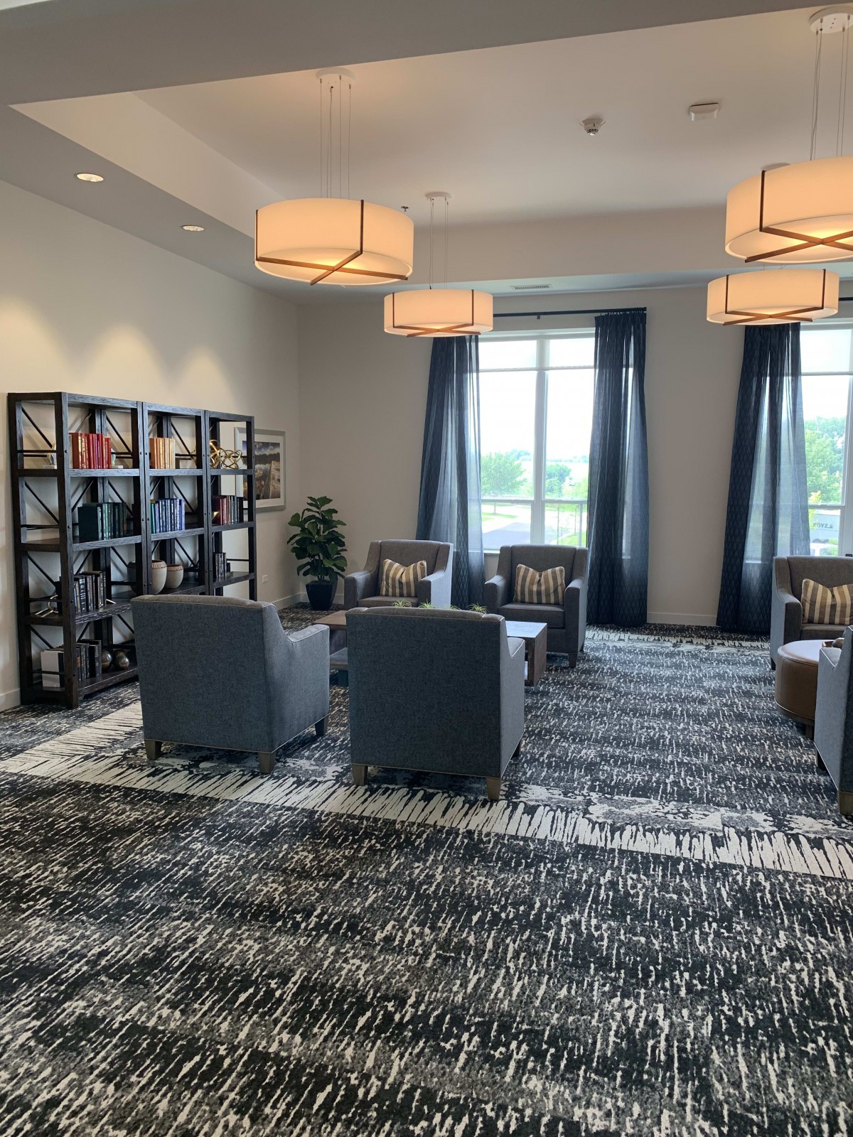 A modern living room with armchairs, a bookshelf, and large windows.