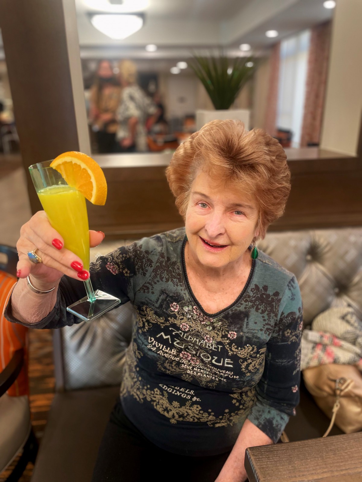 A woman smiling and holding up a drink garnished with an orange slice in celebration.