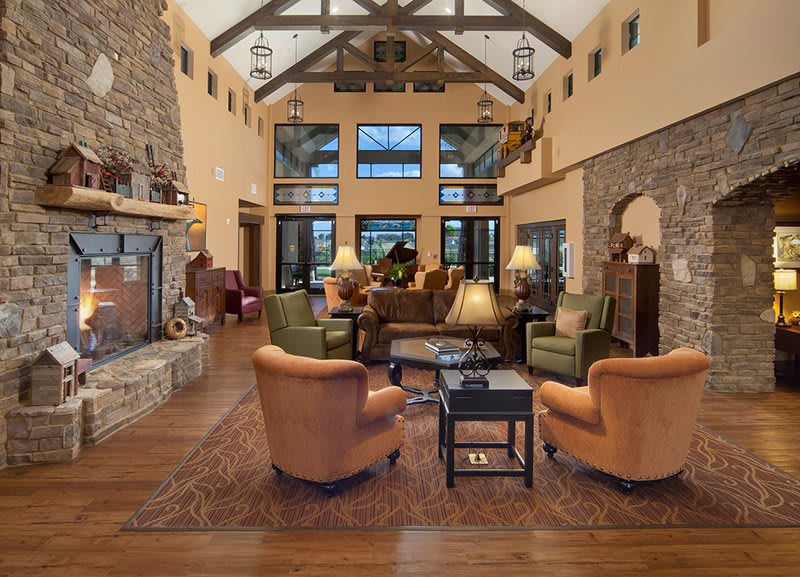 A spacious living room with a rustic design featuring a stone fireplace, high ceilings with wooden beams, and cozy seating arrangements.