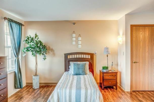 A cozy bedroom with a single bed featuring striped bedding, a wooden nightstand, and a potted plant for decor.