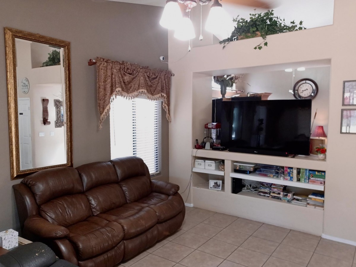 A cozy living room with a brown leather sofa and built-in shelving that houses a television and decorative items.
